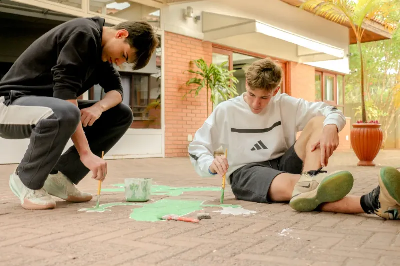 Dois estudantes pintando um desenho no chão do pátio